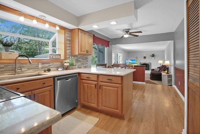 kitchen featuring dishwasher, a sink, a peninsula, light wood finished floors, and a fireplace
