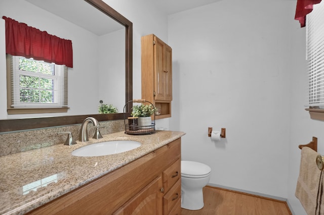half bathroom with wood finished floors, toilet, vanity, and baseboards