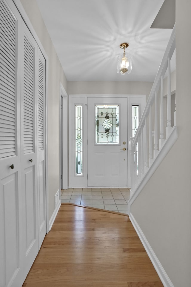 entryway with light wood-type flooring, a chandelier, and baseboards