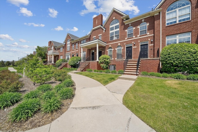 view of property with brick siding, a chimney, cooling unit, and a front lawn