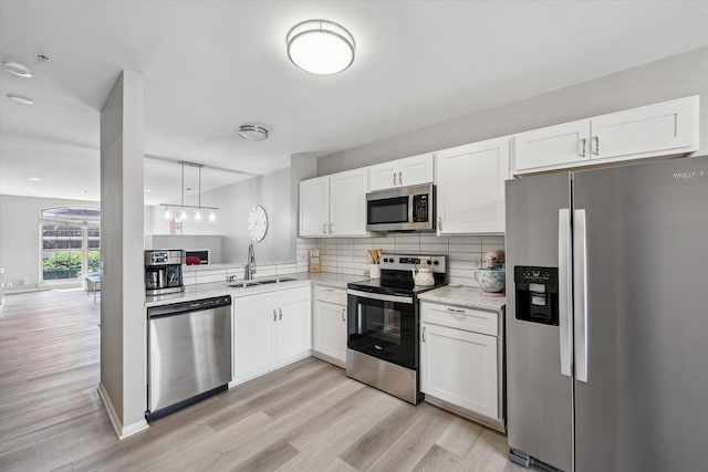 kitchen featuring stainless steel appliances, a sink, light wood-style flooring, white cabinets, and decorative backsplash