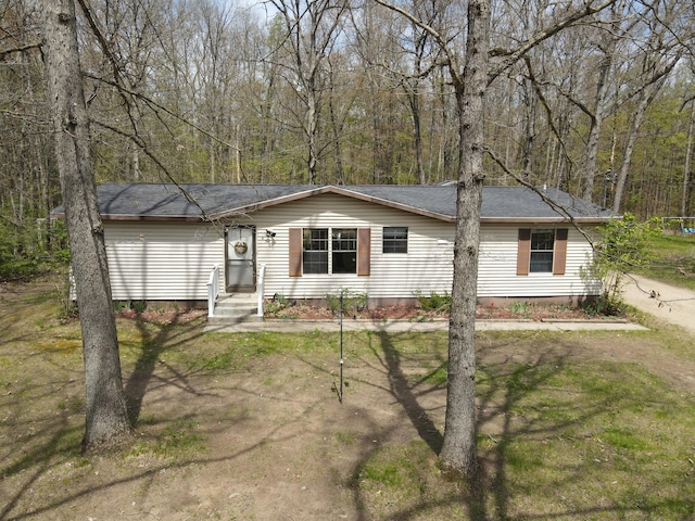 view of front facade with a wooded view, a front lawn, and roof with shingles