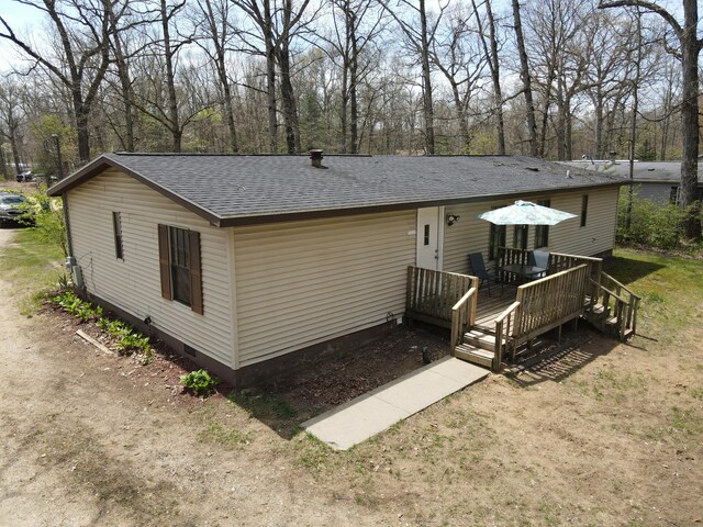 rear view of property featuring roof with shingles, crawl space, a deck, and view of scattered trees