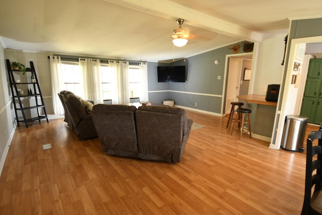 living area featuring beamed ceiling, wood finished floors, a ceiling fan, crown molding, and baseboards