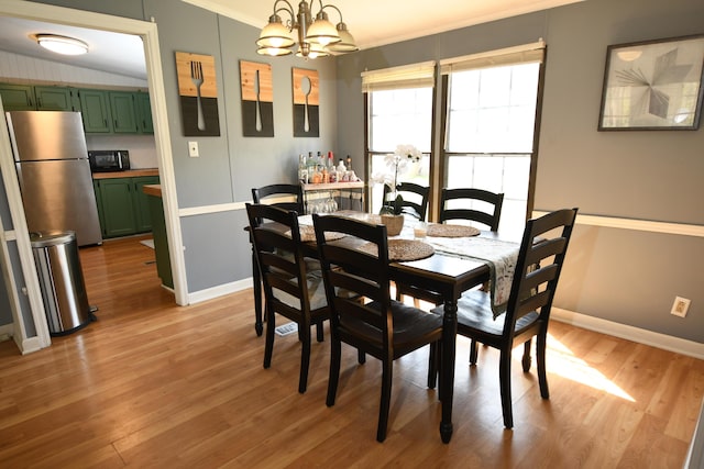 dining space featuring a chandelier, light wood-style flooring, baseboards, vaulted ceiling, and crown molding