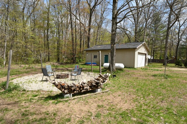 view of grassy yard featuring a fire pit, an outdoor structure, and a garage