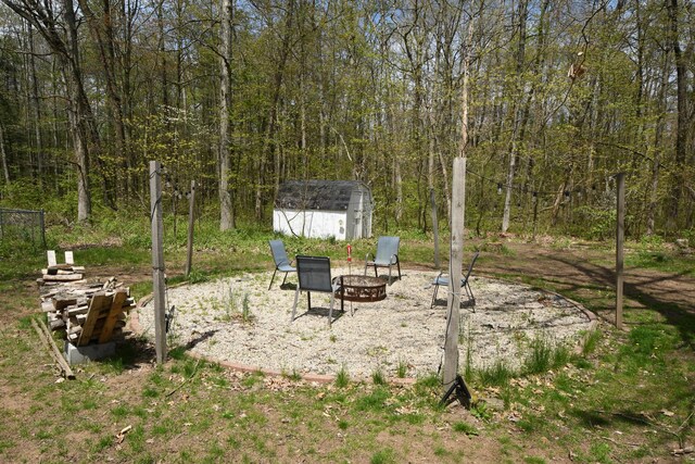 view of yard featuring a fire pit, a storage shed, an outbuilding, and a forest view