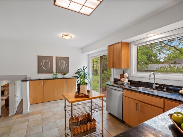 kitchen with a sink, dishwasher, dark stone counters, and light tile patterned flooring