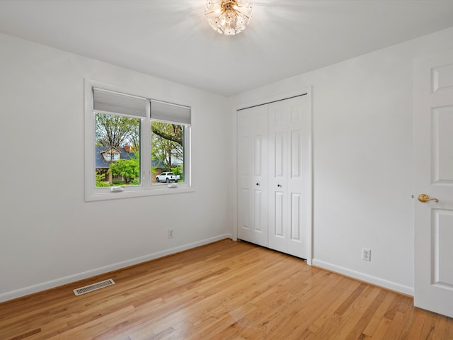 unfurnished bedroom featuring baseboards, light wood-type flooring, a closet, and a chandelier