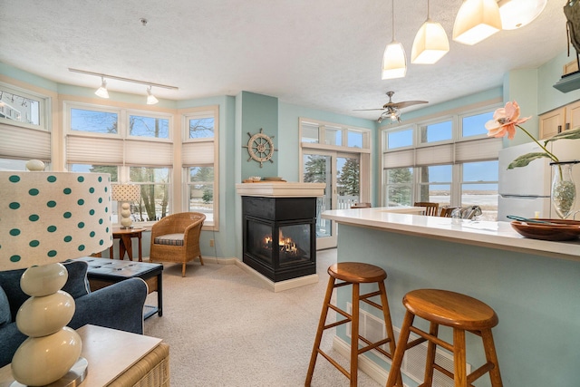 kitchen featuring freestanding refrigerator, track lighting, a multi sided fireplace, light colored carpet, and a ceiling fan