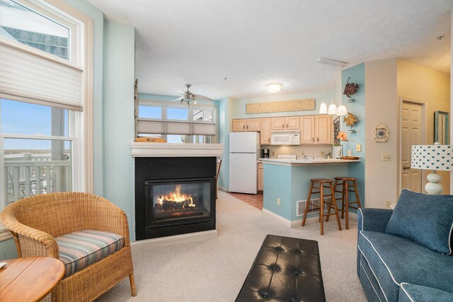 living area with light colored carpet, a glass covered fireplace, a ceiling fan, and baseboards