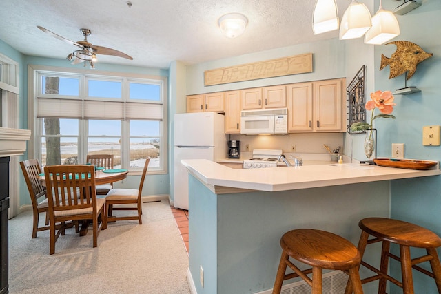 kitchen featuring white appliances, a ceiling fan, baseboards, a breakfast bar, and a peninsula