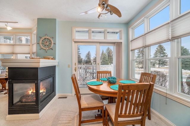 dining area featuring a multi sided fireplace, healthy amount of natural light, baseboards, and carpet floors