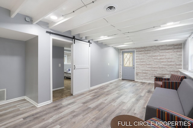 below grade area with a barn door, baseboards, an accent wall, and light wood finished floors