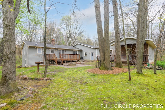 back of property featuring a deck, a chimney, and a lawn