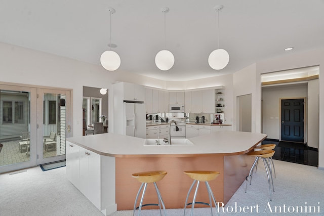 kitchen featuring white appliances, light countertops, light carpet, and a kitchen breakfast bar