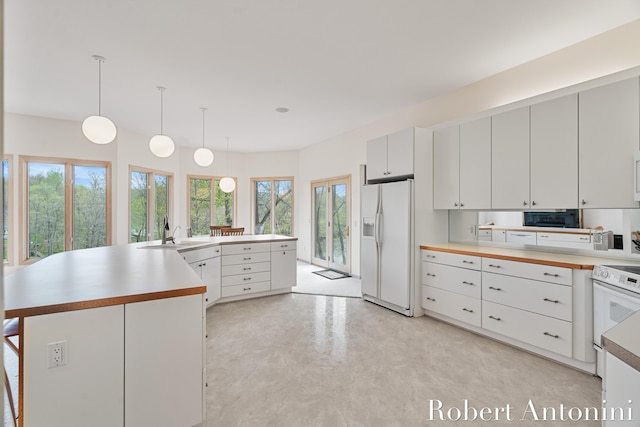 kitchen featuring white appliances, a sink, light countertops, pendant lighting, and white cabinets