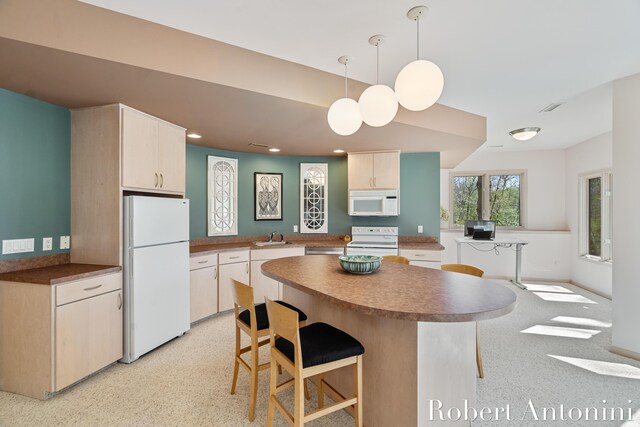 kitchen with white appliances, a sink, a breakfast bar area, dark countertops, and pendant lighting