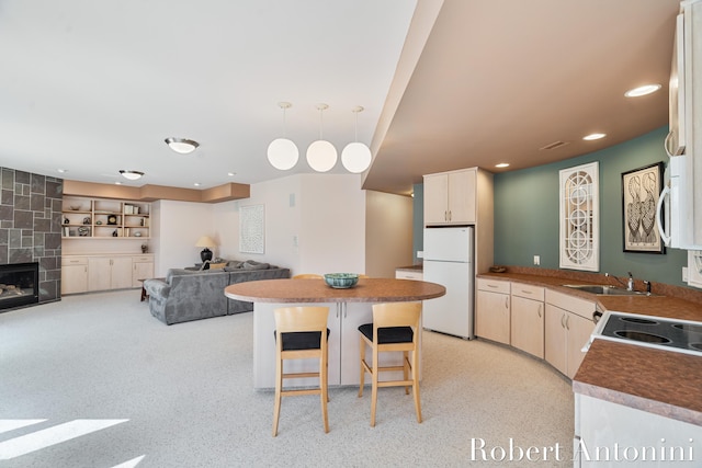 kitchen featuring white appliances, a sink, hanging light fixtures, a fireplace, and a breakfast bar area