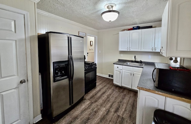 kitchen with appliances with stainless steel finishes, a sink, dark countertops, white cabinetry, and ornamental molding