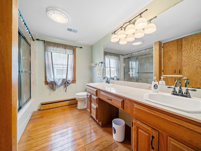 4825 Downing Dr, Pinckney, MI 48169 - full bathroom featuring baseboard heating, toilet, hardwood / wood-style floors, double vanity, and bath / shower combo with glass door