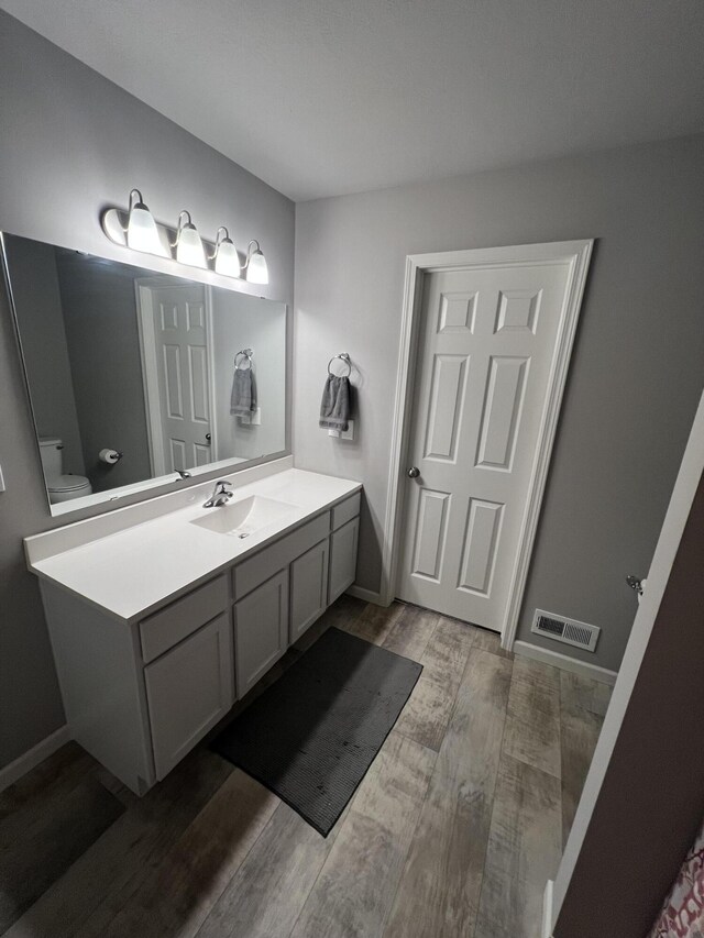 bathroom with wood finished floors, vanity, toilet, and baseboards