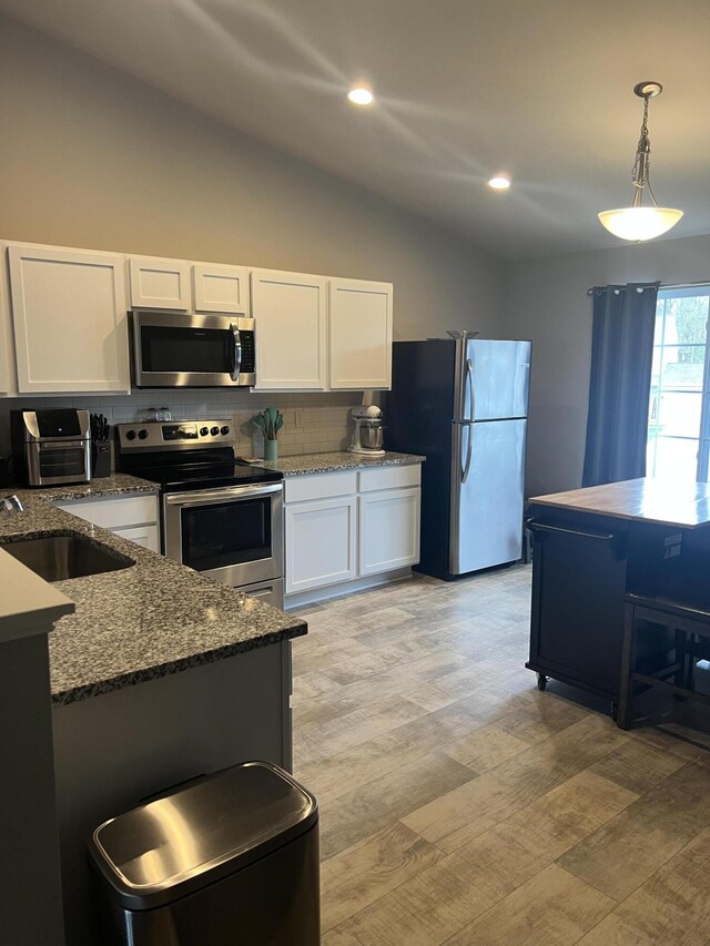 kitchen featuring stainless steel appliances, a sink, lofted ceiling, tasteful backsplash, and white cabinets
