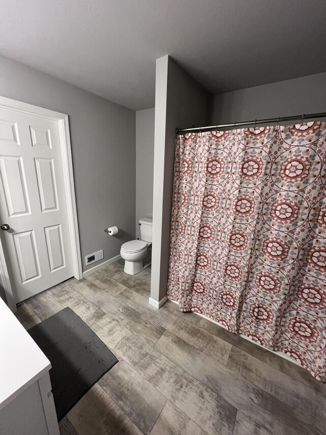 bathroom with wood finished floors, toilet, baseboards, vanity, and curtained shower
