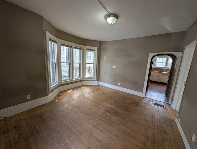 empty room featuring wood-type flooring, baseboards, and arched walkways