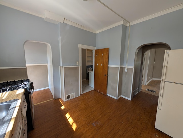 kitchen with freestanding refrigerator, arched walkways, wood finished floors, ornamental molding, and a wainscoted wall