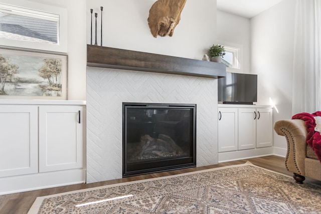 detailed view of wood finished floors, a glass covered fireplace, and baseboards