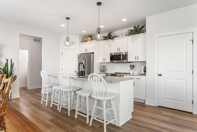 kitchen featuring stainless steel appliances, a center island with sink, backsplash, a kitchen bar, and white cabinets