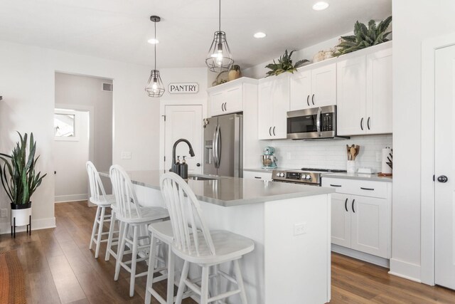 kitchen featuring appliances with stainless steel finishes, a kitchen island with sink, tasteful backsplash, a kitchen bar, and white cabinets