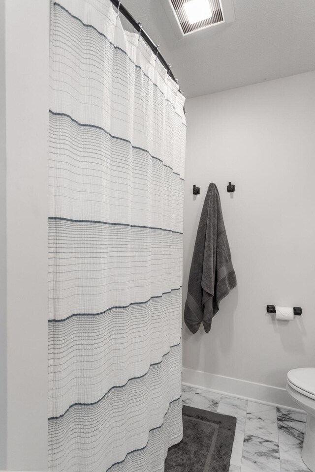 bathroom featuring marble look tile flooring, toilet, baseboards, and a shower with curtain