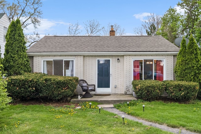 view of front of house featuring brick siding, a chimney, a front yard, and a shingled roof