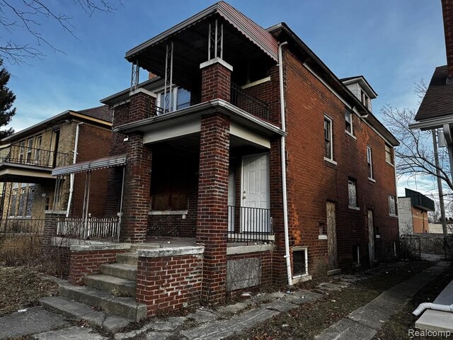 view of front of property with a balcony, brick siding, and covered porch