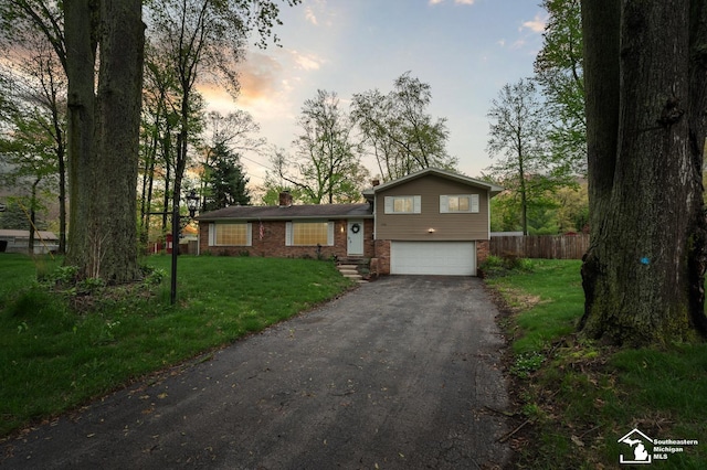 split level home with brick siding, asphalt driveway, a garage, and a chimney