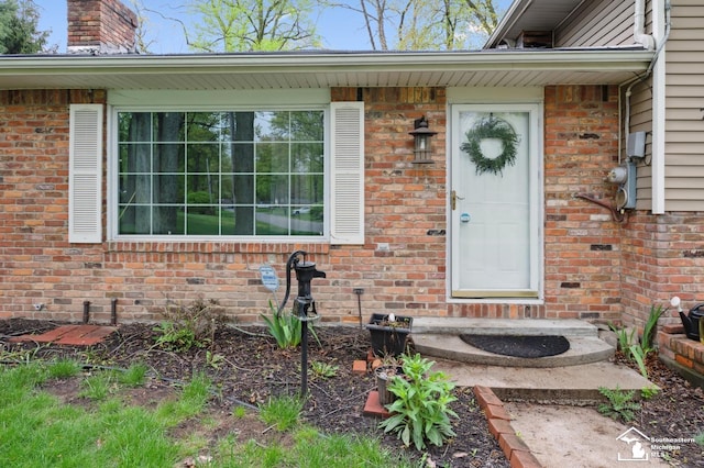view of exterior entry featuring a chimney and brick siding