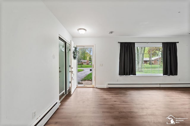 empty room with a baseboard radiator, plenty of natural light, wood finished floors, and a baseboard heating unit