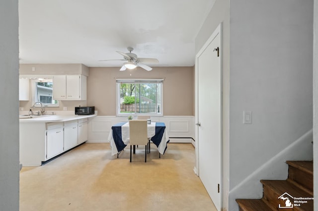 kitchen featuring black microwave, a sink, healthy amount of natural light, white cabinets, and a wainscoted wall