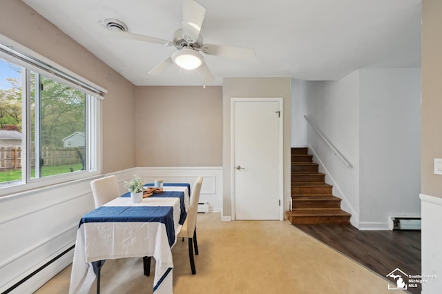 dining area with a baseboard radiator, a baseboard heating unit, wainscoting, stairs, and a ceiling fan
