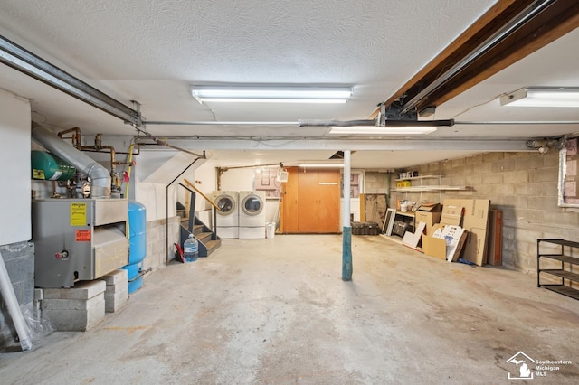 unfinished basement featuring washing machine and clothes dryer, a water pressure tank, concrete block wall, and a textured ceiling