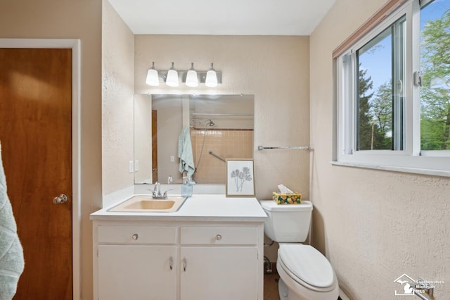 bathroom with plenty of natural light, toilet, vanity, a textured wall, and a shower