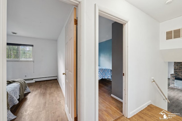 hall with wood finished floors, an upstairs landing, and baseboard heating