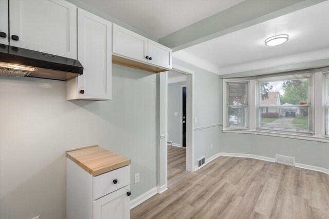 kitchen featuring light wood-type flooring, under cabinet range hood, white cabinetry, baseboards, and light countertops