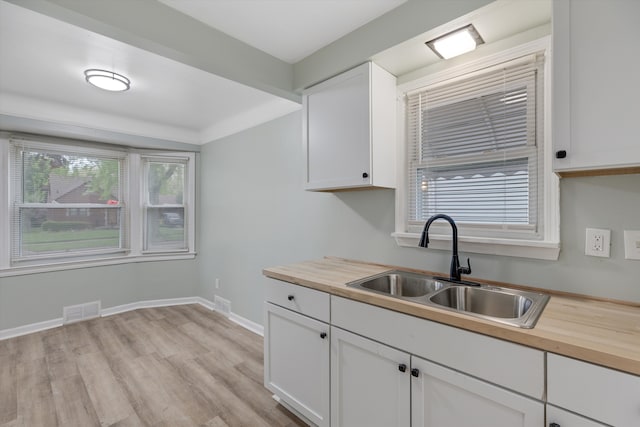 kitchen with wood counters, a sink, light wood finished floors, white cabinets, and baseboards