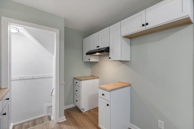 kitchen featuring light wood-type flooring, under cabinet range hood, wood counters, white cabinets, and baseboards