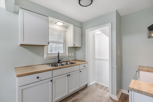 kitchen featuring butcher block countertops, a sink, light wood finished floors, white cabinetry, and baseboards