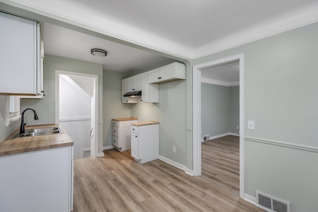 kitchen featuring a sink, light wood-style flooring, white cabinetry, under cabinet range hood, and butcher block counters