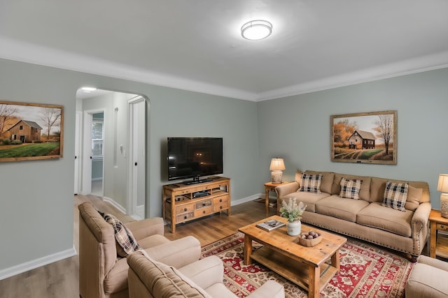 living area featuring wood finished floors, baseboards, arched walkways, and crown molding
